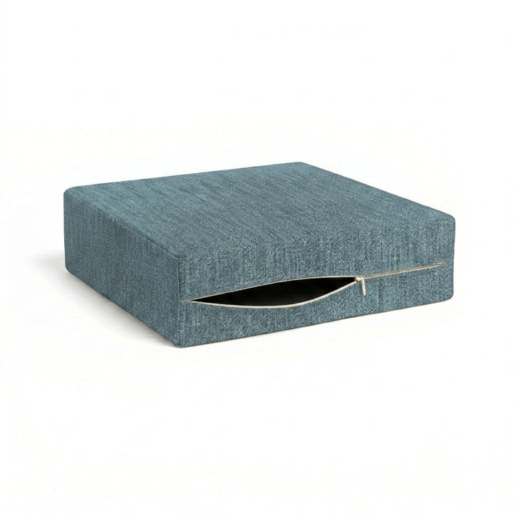 A square upholstered ottoman or cushion in textured blue-gray fabric, shown closed on a clean white background.