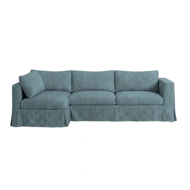 A three-seat slipcovered sofa in a textured slate blue fabric, featuring a single matching throw pillow, a skirted base, and wide armrests, shown against a plain white background.